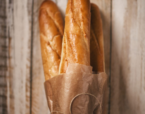 Fresh baguettes in paper on wooden background