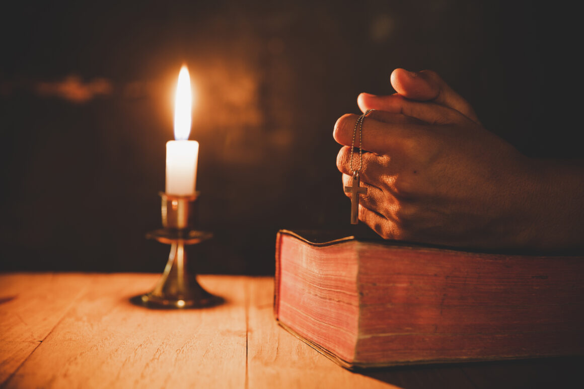 Close up man's hand is praying in the Church with lit candle, re Refleksja duchowa