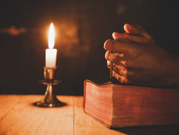 Close up man's hand is praying in the Church with lit candle, re Refleksja duchowa