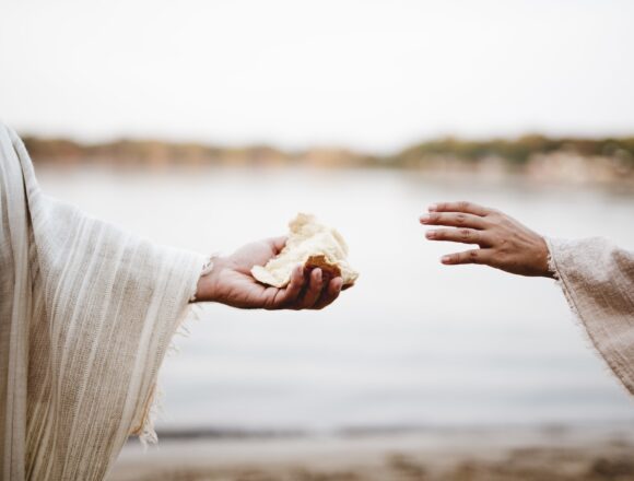 Closeup shot of a person wearing a biblical robe giving bread to another person Post – duchowe i zdrowotne korzyści umiarkowania