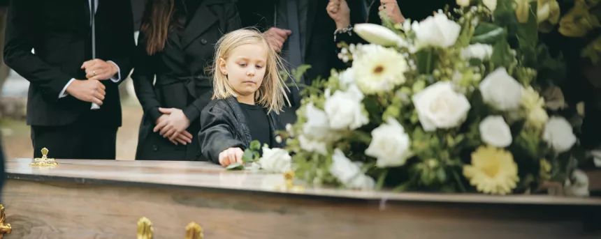 Death, grief and girl at funeral with flower on coffin, family and sad child at service in graveyard for respect. Roses, loss and people at wood casket in cemetery with kid crying at grave for burial Jak rozmawiać z dziećmi o śmierci?